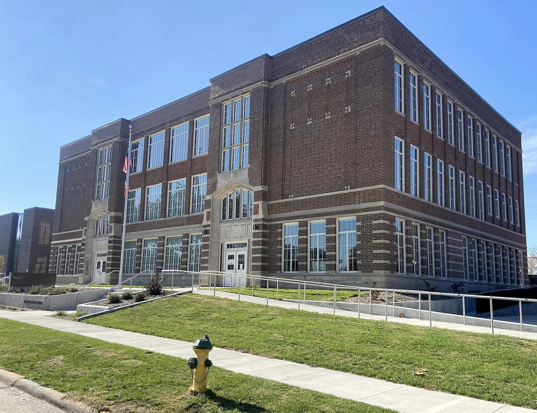 The Neveln Center, a restored three-storey brick school building from 1919, with a lawn and sidewalk under a blue sky