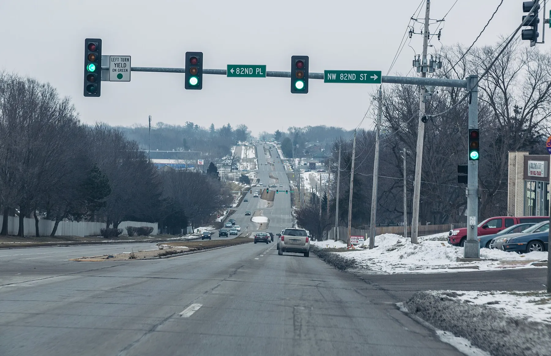 Traffic lights over Hickman Road at NW 82nd Street in Clive, with snow along the curb and the road running on into the distance