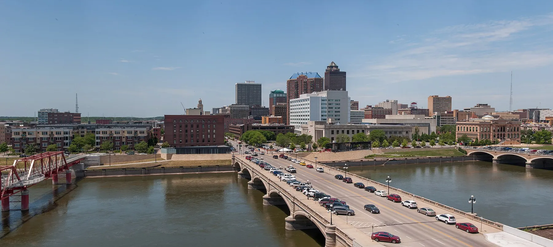 Downtown Des Moines skyline beyond the Des Moines River and a busy road bridge on a clear summer day