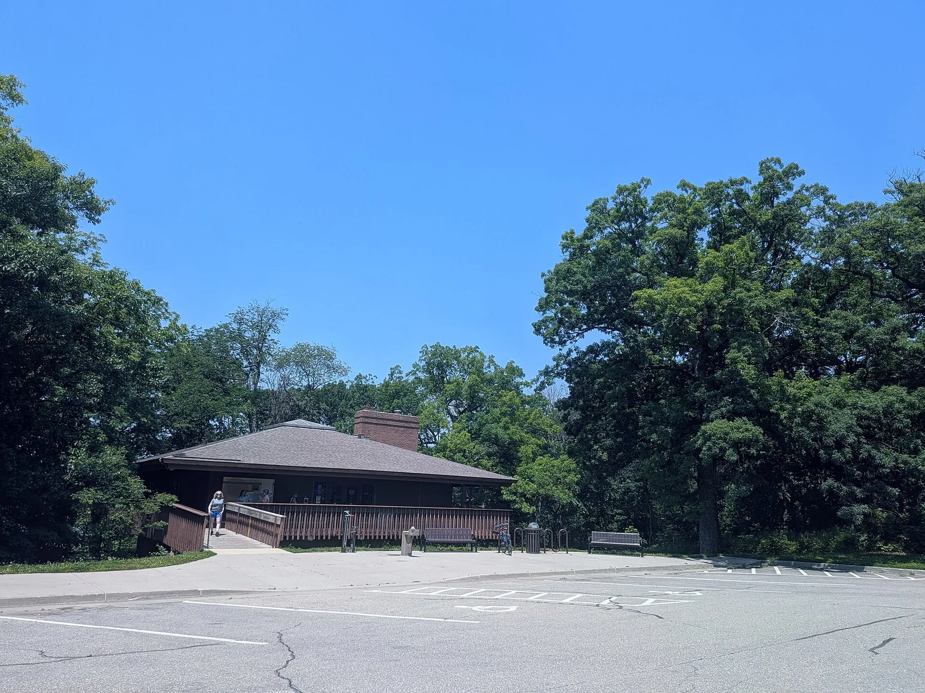 A low brown-roofed visitor center among mature oaks at Saylorville Lake, with a footbridge and a parking lot in front