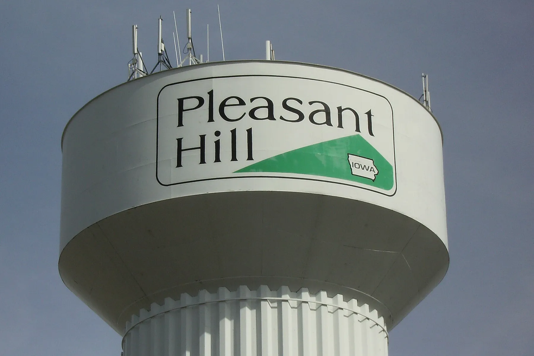 The top of the Pleasant Hill water tower, painted with the city's name and a green Iowa emblem, against a gray sky