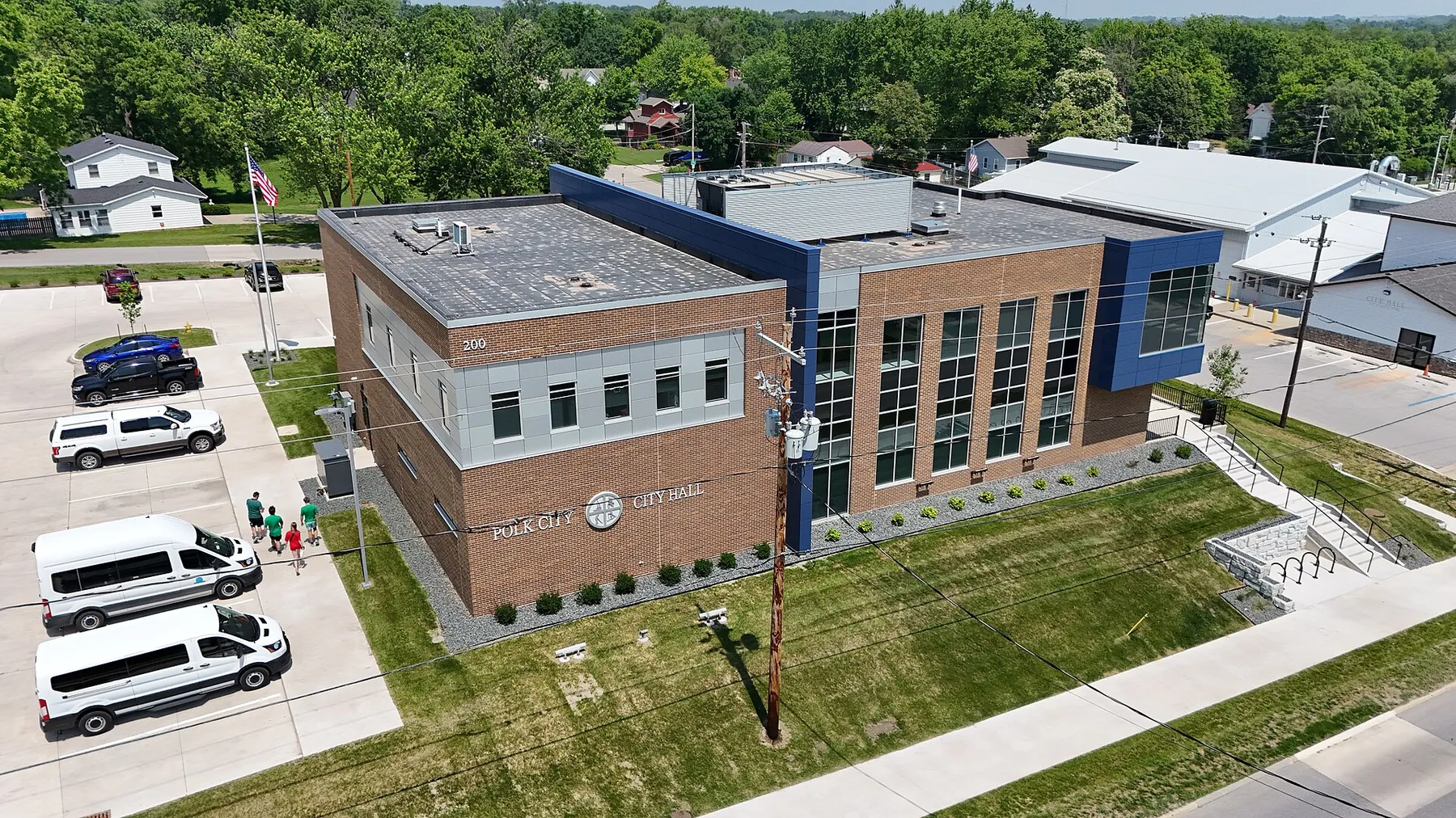Aerial view of the brick Polk City City Hall with a lawn and parking lot, and houses among trees behind
