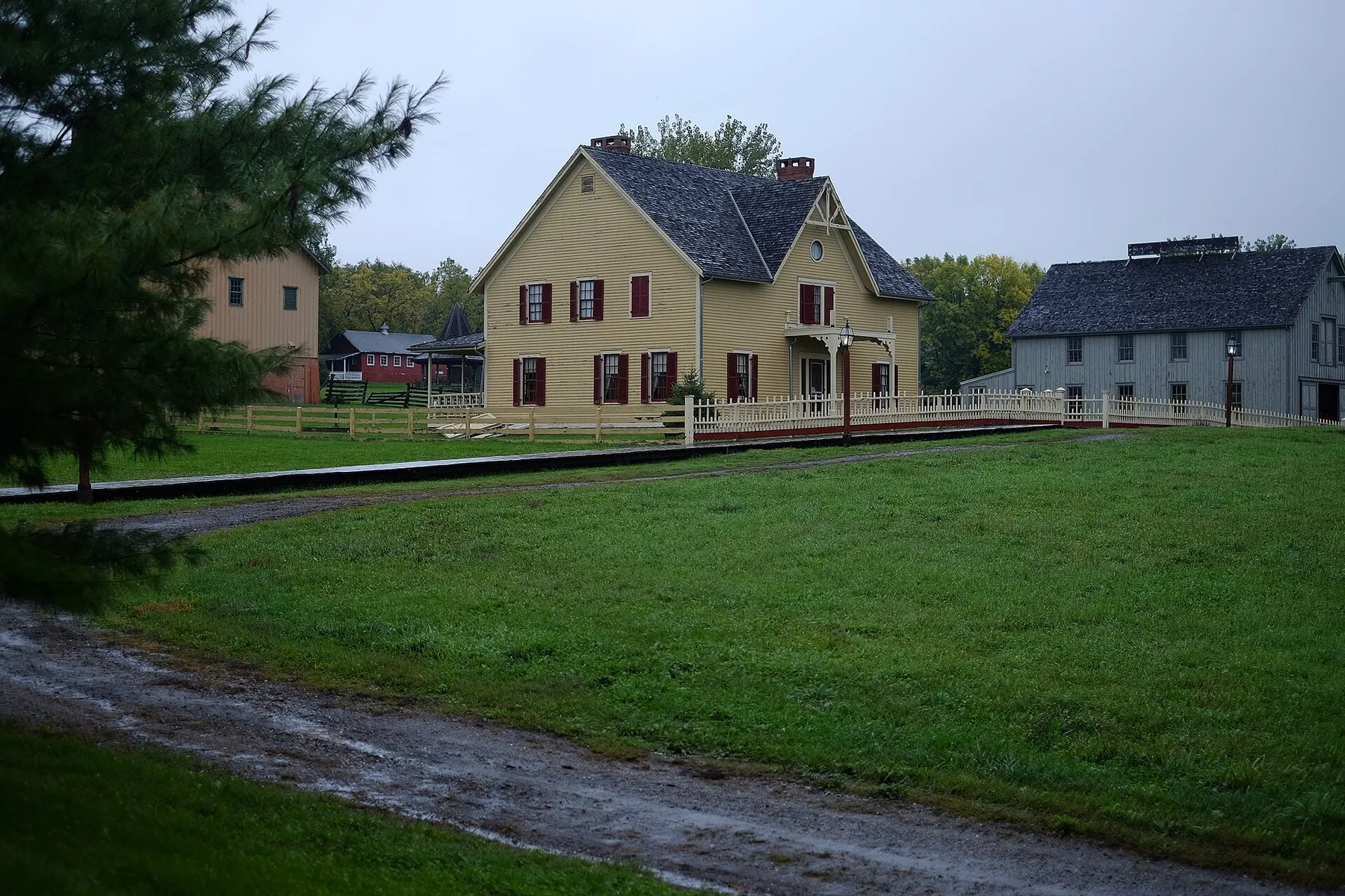 A yellow two-storey 1870s-style farmhouse and outbuildings behind a white fence and a broad lawn at Living History Farms