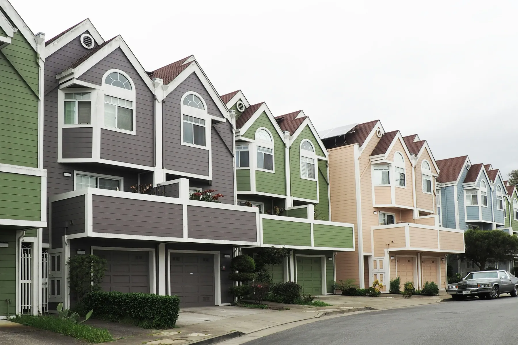 A row of attached two- and three-storey townhomes in green, grey, tan and blue siding with bay windows and garages